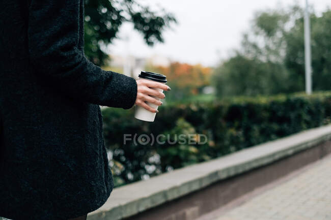 Femme marchant le long de la rue avec une tasse de café jetable — Photo de stock