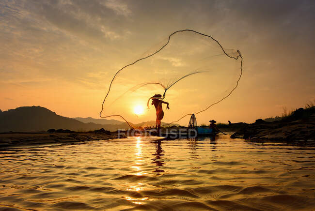 Silhouette eines Fischers, der Fischernetze in einen Fluss wirft, Thailand — Stockfoto
