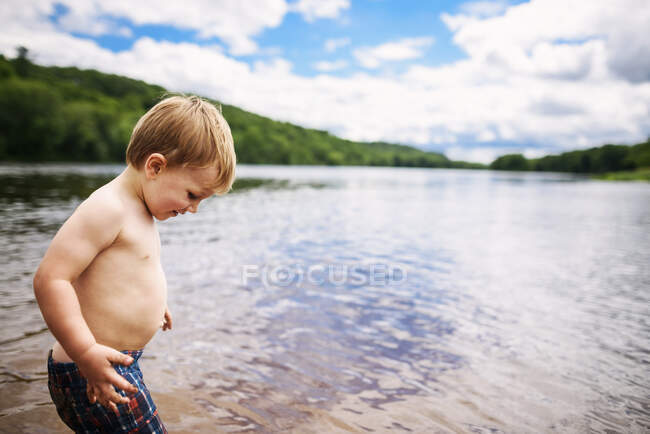 Retrato de un niño de pie junto a un río en el verano - foto de stock