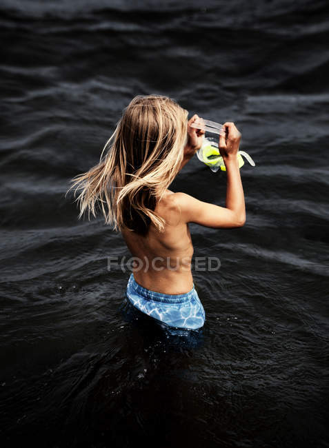 Fille aux cheveux longs debout dans la mer tenant des lunettes de natation — Photo de stock