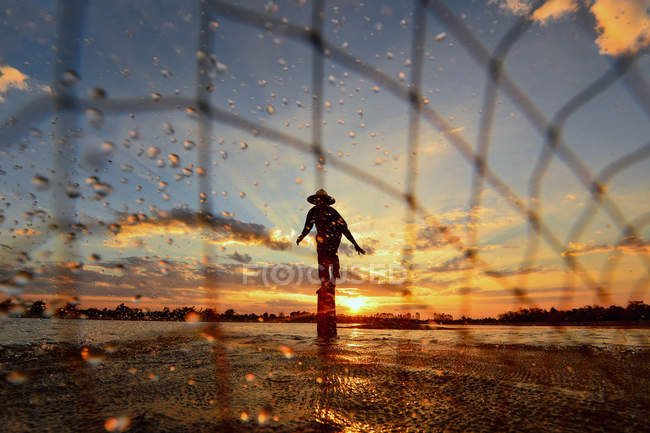Silhueta de pescador rede de pesca na água ao pôr do sol, Tailândia — Fotografia de Stock