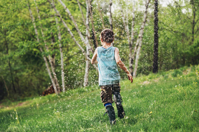 Мальчик бежит через разбрызгиватель в саду — стоковое фото