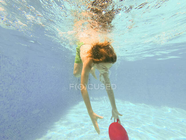 Boy diving underwater in a swimming pool to get a red balloon — Stock Photo