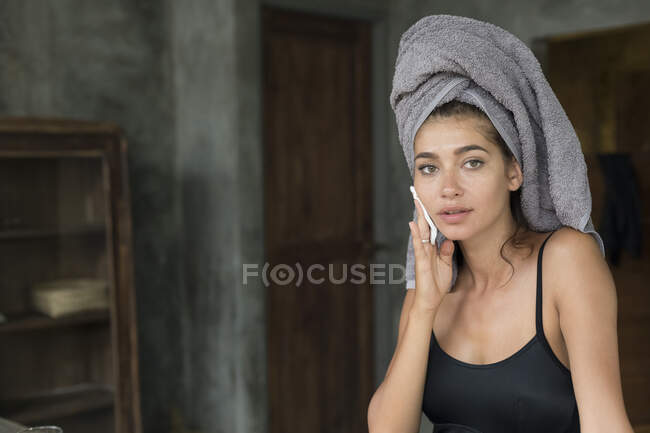 A young woman wearing a grey head towel is preparing for her facemask after a shower in a tropical balinese villa. — Fotografia de Stock