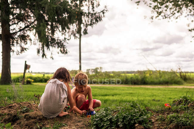 Two young children playing with cars in the dirt — Stock Photo