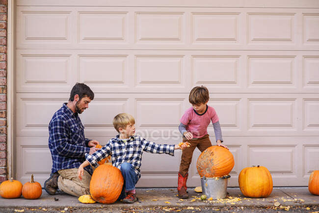 Deux enfants et un père sculptant des citrouilles — Photo de stock