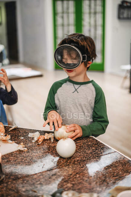 Молодий хлопчик допомагає різати цибулю на кухні — стокове фото