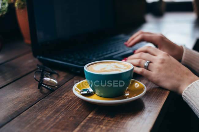 Copa de café al lado de una mujer que usa el ordenador portátil - foto de stock