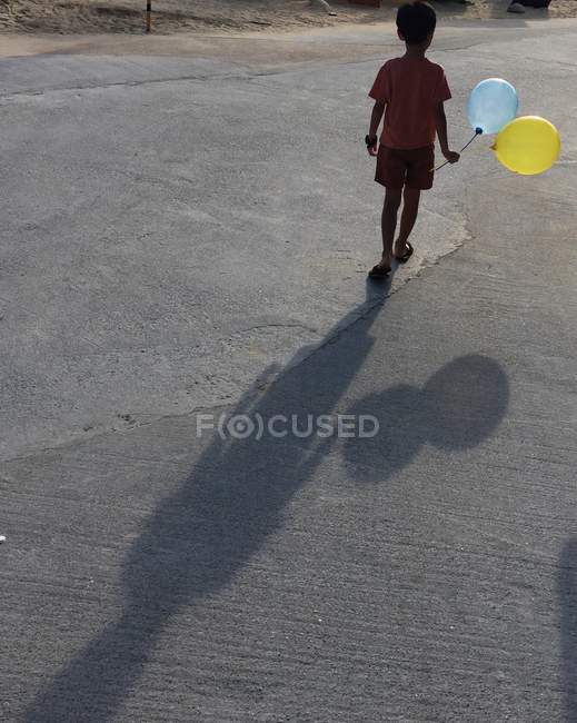 Niño de pie en la calle sosteniendo globos - foto de stock