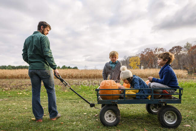 Three kids riding on a wagon with pumpkins in a pumpkin patch — Stock Photo