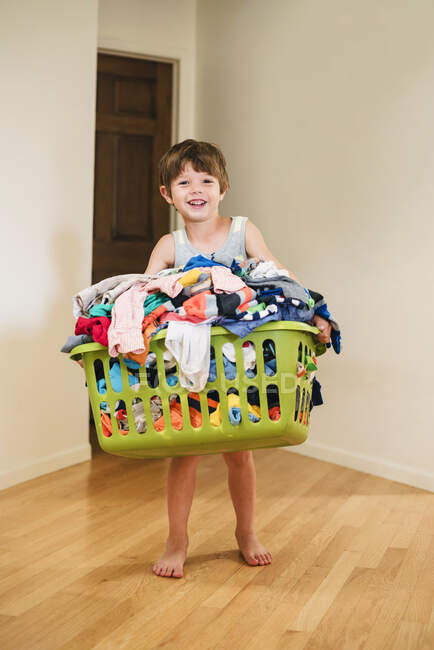 Улыбающийся мальчик с корзиной для белья, наполненной одеждой — стоковое фото
