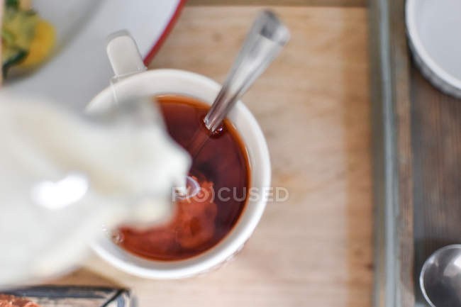 Milch in eine Tasse Tee gießen — Stockfoto