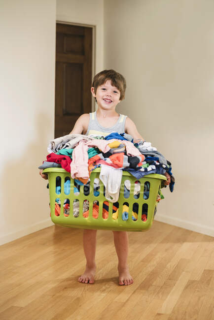Smiling Boy carrying laundry basket filled with clothes — Stock Photo