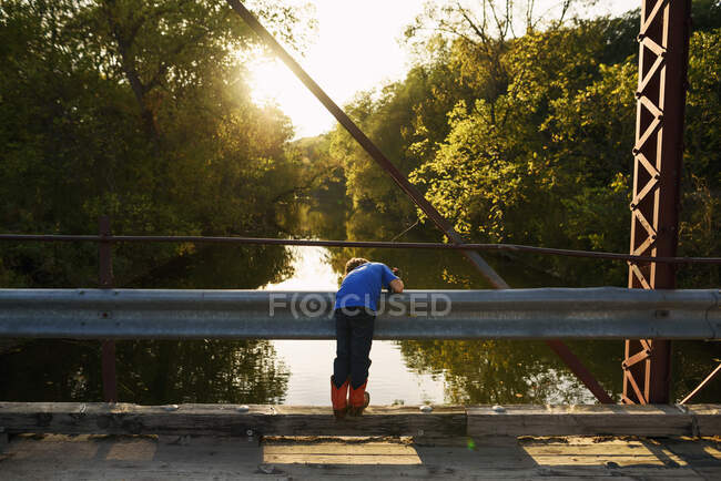 Молодий хлопчик рибалить з мосту під вечірнім сонцем — стокове фото