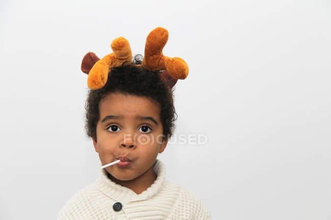 Портрет улыбающегося мальчика с рождественскими рогами, поедающего леденец — стоковое фото