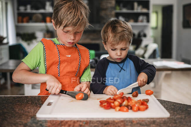 Dos niños pequeños ayudando a cocinar en la cocina - foto de stock