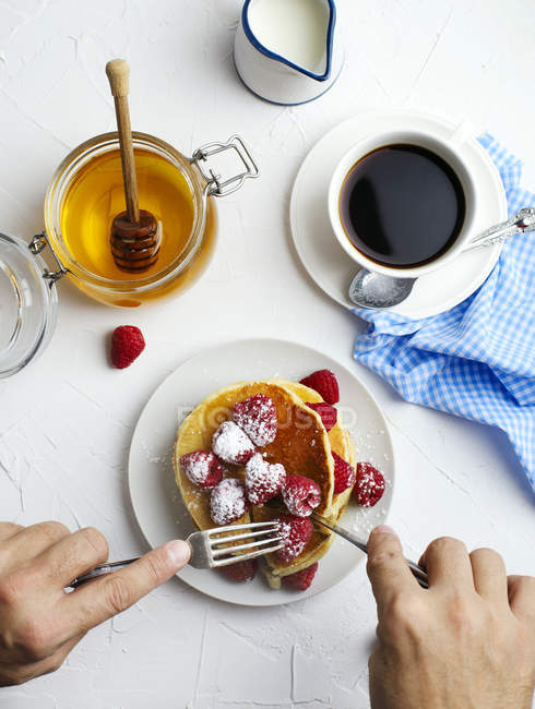 Mann isst Pfannkuchen mit frischen Himbeeren und Honig zum Frühstück. , Ansicht von oben — Stockfoto