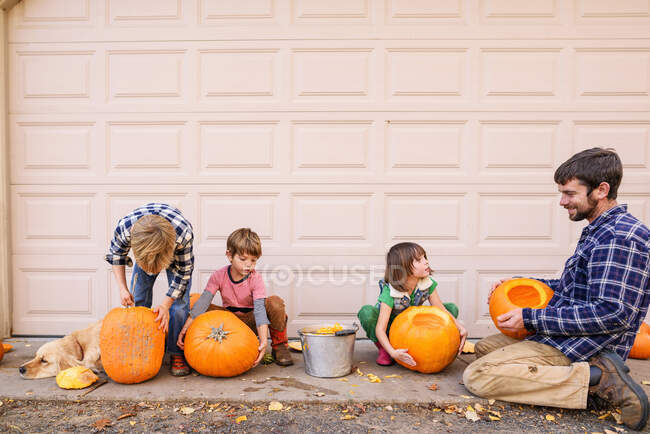 Tres hijos y un padre tallando calabazas - foto de stock