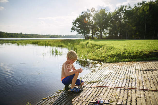 Jeune garçon pêche dans un lac paisible avec reflet du ciel et des nuages — Photo de stock