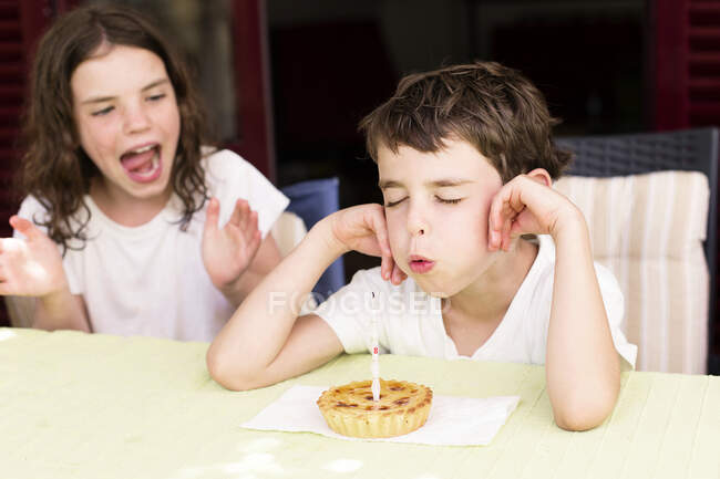 Junge bläst Geburtstagskerze aus, seine Schwester sitzt neben ihm und klatscht — Stockfoto