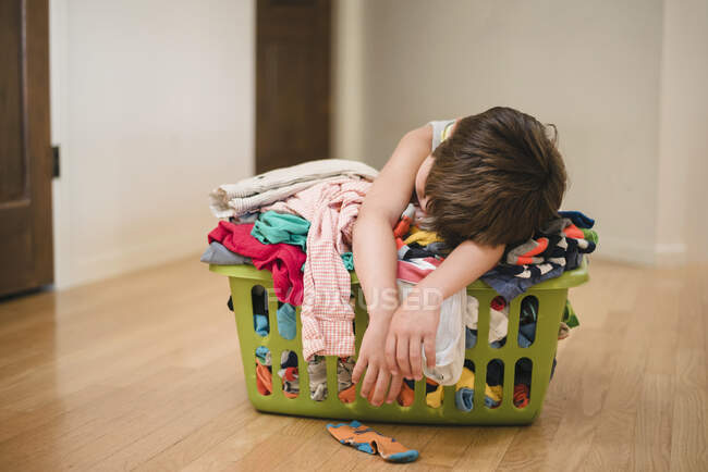 Хлопчик спить на пральні, наповненій одягом — стокове фото