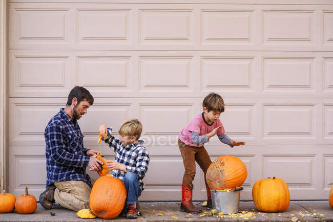 Dos hijos y un padre tallando calabazas - foto de stock