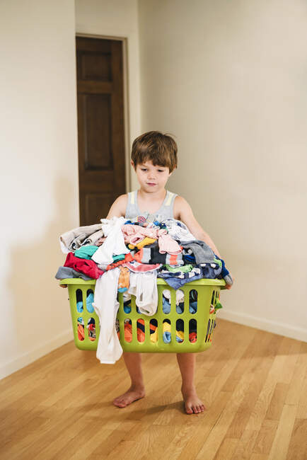 Хлопчик носить кошик для білизни, наповнений одягом — стокове фото