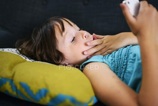 Девушка лежит на диване и смотрит на свой мобильный телефон. — стоковое фото