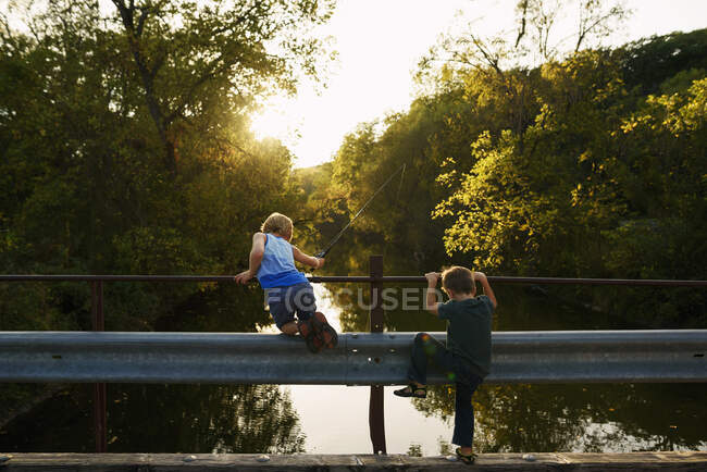 Двоє хлопчиків рибалять з мосту під вечірнім сонцем — стокове фото