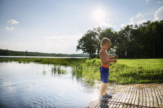 Niño pescando en un lago tranquilo con reflejo del cielo y las nubes - foto de stock