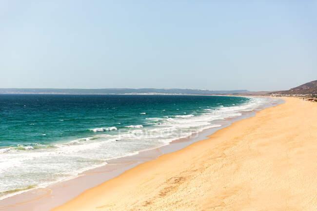 Playa de arena con olas y cielo azul - foto de stock