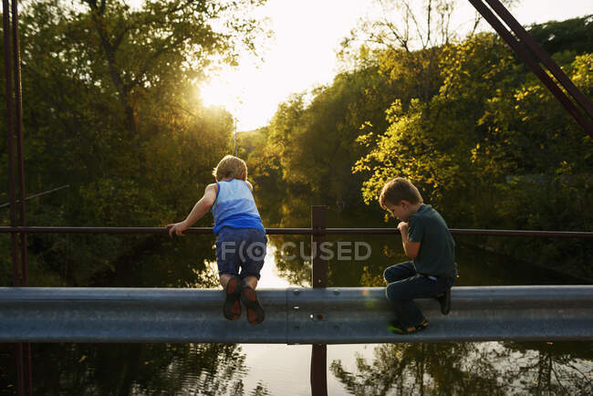 Two young boy fishing off of a bridge in the evening sun — Stock Photo