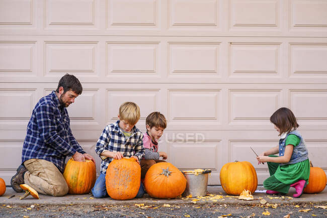 Tres hijos y un padre tallando calabazas - foto de stock