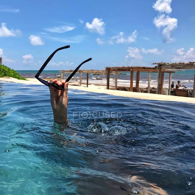 Jeune femme sous l'eau dans une piscine tenant des lunettes de soleil au-dessus de l'eau — Photo de stock