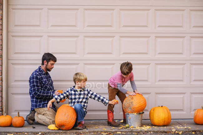 Zwei Kinder und ein Vater schnitzen Kürbisse — Stockfoto