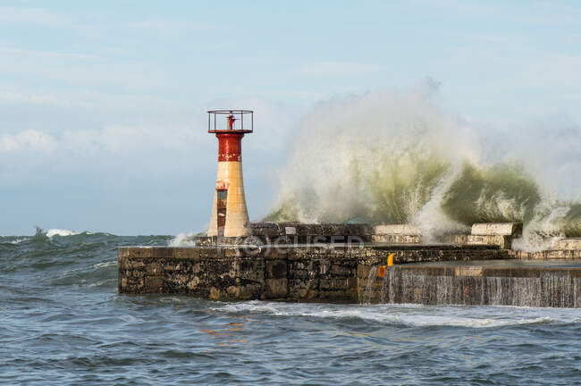 Lighthouse with breaking storm wave at pier — Stock Photo