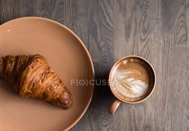 Taza de café y croissant sobre mesa de madera - foto de stock