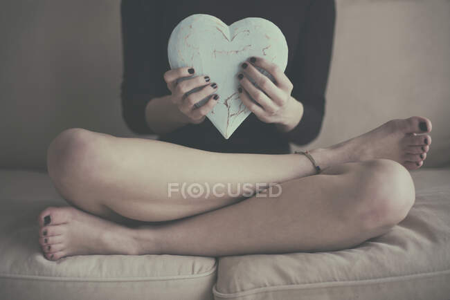 Young woman sitting on sofa and holding heart — Stock Photo