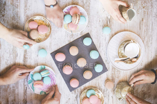 Vista dall'alto delle mani con macaron colorati su tavolo di legno — Foto stock
