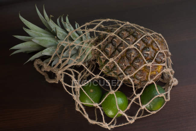Vista close-up de abacaxi e limas em um saco de malha — Fotografia de Stock