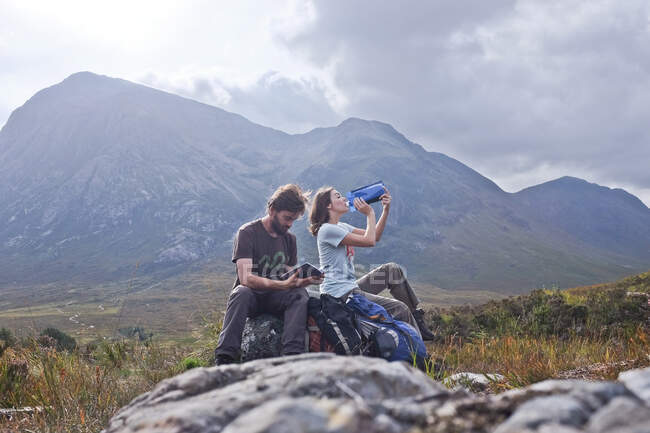 Пара сидящих на скале питьевой воды и глядя на путеводитель, Шотландия, Англия, Великобритания — стоковое фото