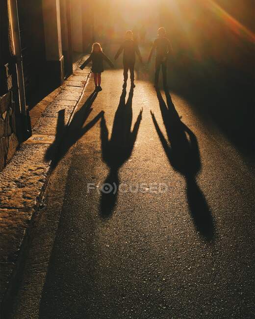 Tres niños caminando por la calle tomados de la mano - foto de stock
