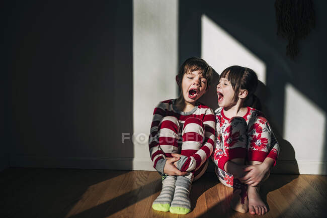 Niño y niña sentados en el suelo bostezando - foto de stock