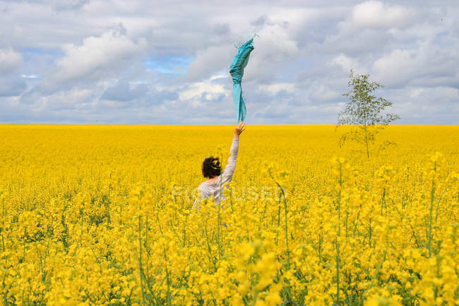 Woman standing in a rapeseed field waving a scarf in the air, Niort, Nouvelle-Aquitaine, France — Stock Photo