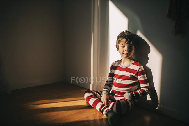 Garçon assis sur le sol appuyé contre un mur — Photo de stock