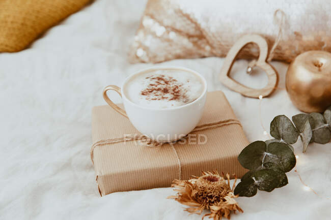 Cappuccino e uma caixa de presente embrulhada em uma cama — Fotografia de Stock