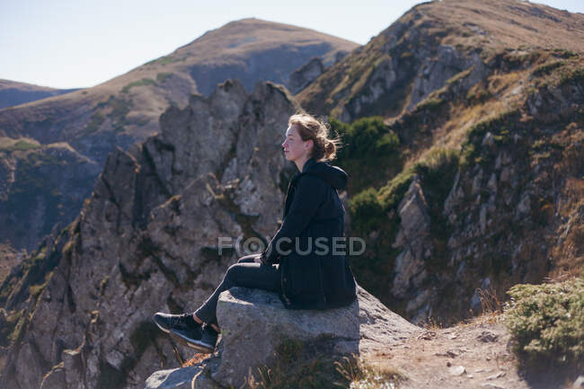 Mujer sentada en un acantilado mirando a la vista de la montaña, Ucrania - foto de stock