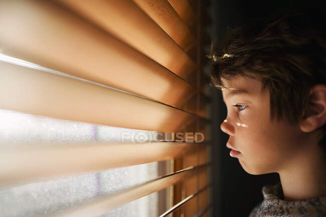 Ragazzo in piedi vicino a una finestra che guarda attraverso le tende — Foto stock