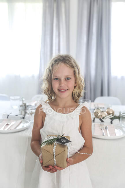 Girl standing by a dining table holding a Christmas gift - foto de stock