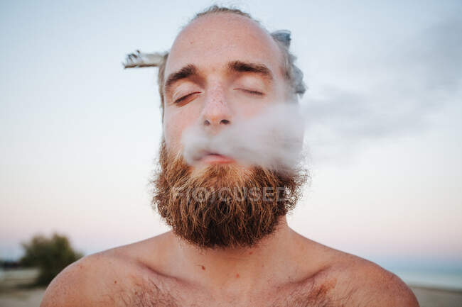 Retrato de un hombre con una pluma en el pelo fumando - foto de stock